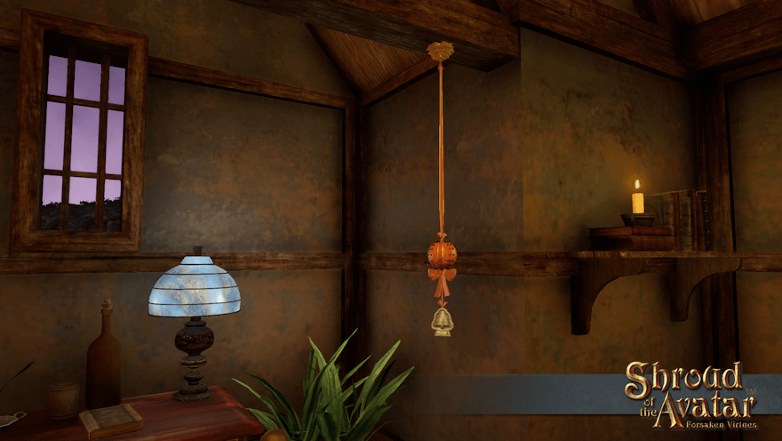 A cloved orange pomander, tied with a red ribbon and with a silver bell of courage ornament below it, hangs by a desk from a rafter in a small Benefactor home.