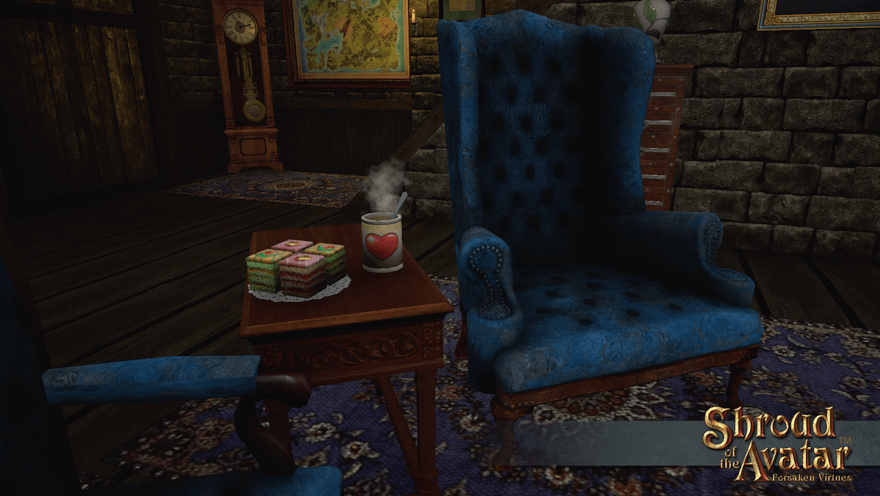 A steaming stoneware mug with a spoon in it and a heart on the front sits next to petit fours on a table between two fireside velvet armchairs.