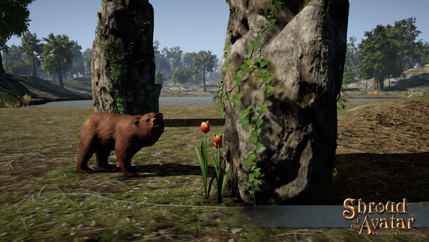 A brown bear looks at you beside a few large stones and a small patch of orange tulips by a forest lake.